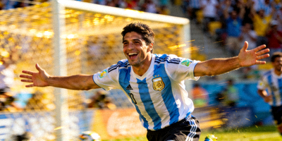 世界杯金靴奖得主在比赛中庆祝进球 - 球员奔跑欢呼，背景是模糊的球场和观众